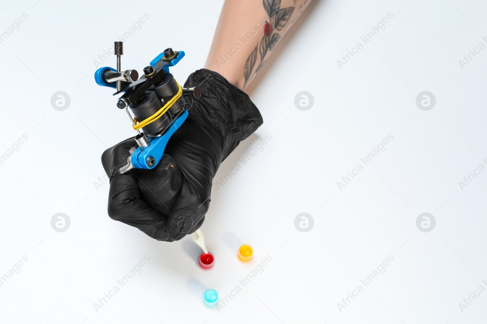 Photo of Tattoo artist with professional machine and colorful ink on white background, closeup