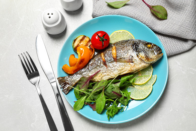Photo of Delicious roasted fish with lemon and vegetables on grey marble table, flat lay