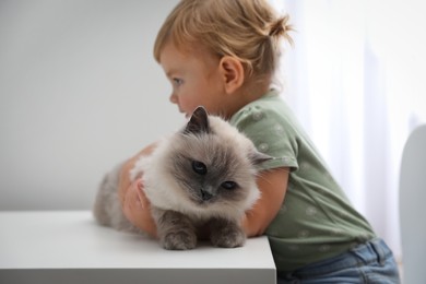 Photo of Cute little child with adorable pet at white table in room