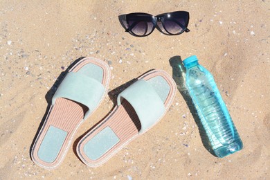 Photo of Stylish sunglasses, slippers and bottle of water on sand. Beach accessories