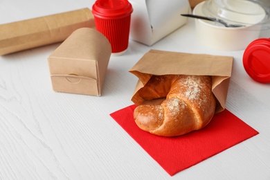 Paper bag with pastry and takeaway food on wooden table