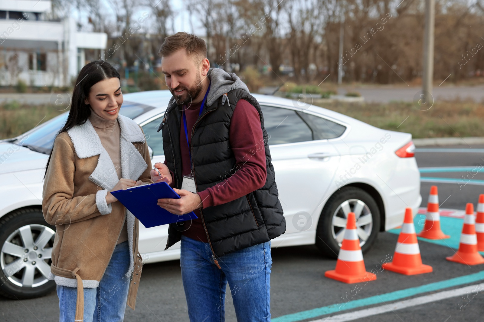 Photo of Young woman with instructor near car at driving school test track