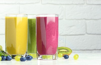 Photo of Fresh colorful fruit smoothies and ingredients on table against white brick wall. Space for text