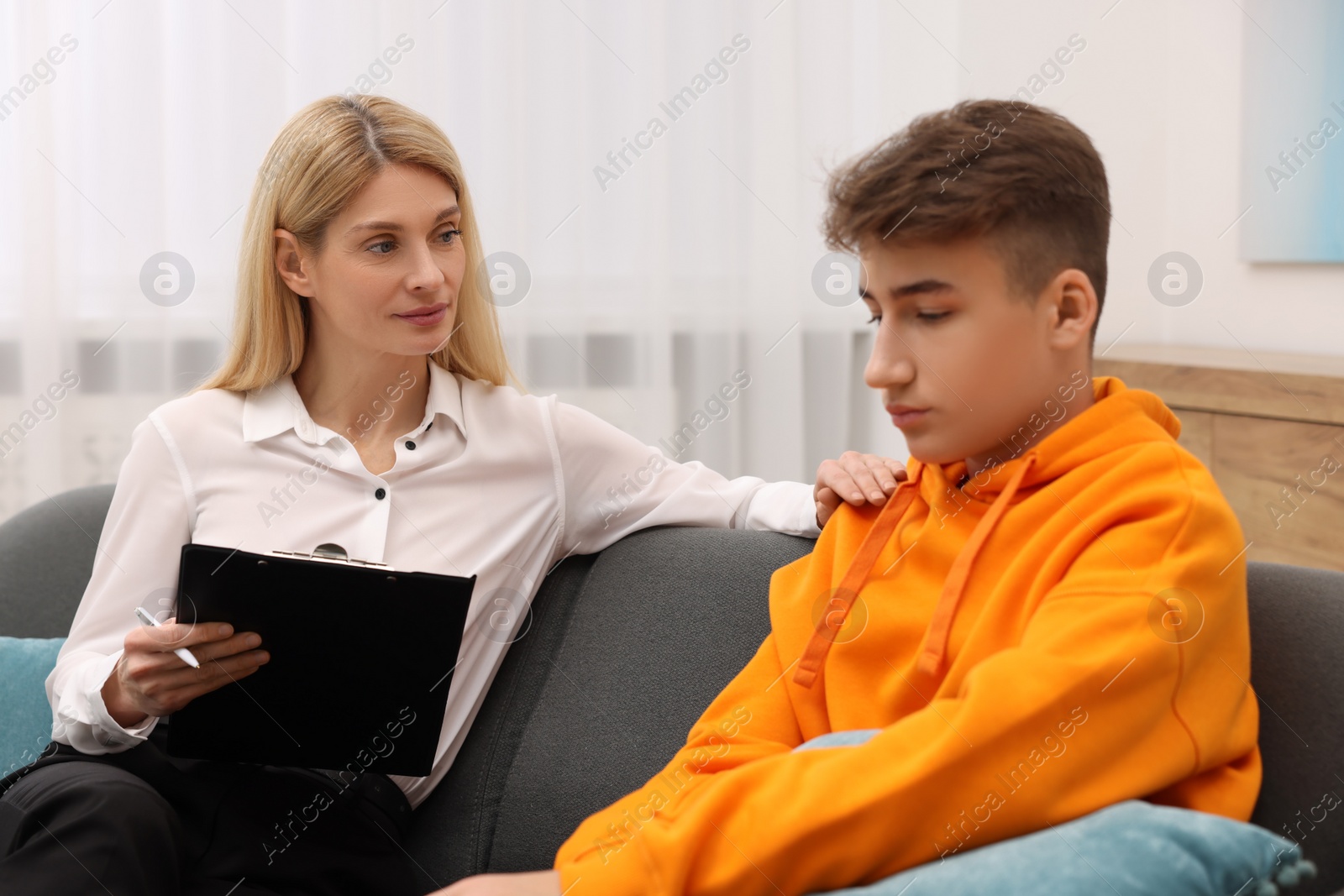 Photo of Psychologist working with teenage boy on sofa in office