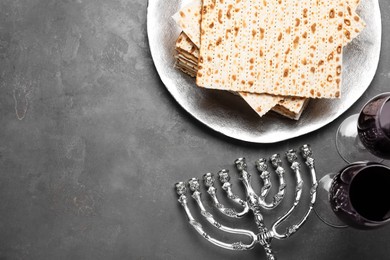 Photo of Matzos, red wine and menorah on grey table, flat lay. Space for text
