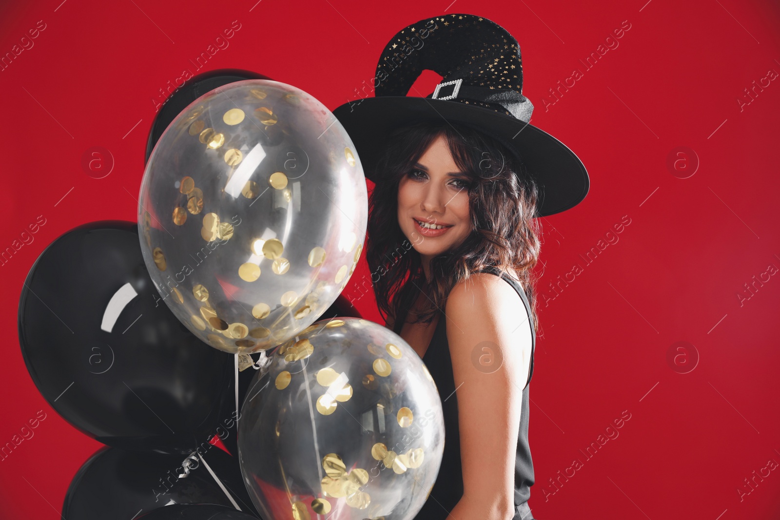 Photo of Beautiful woman in witch costume with balloons on red background. Halloween party