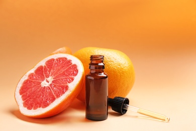 Bottle of essential oil and fresh grapefruits on color background