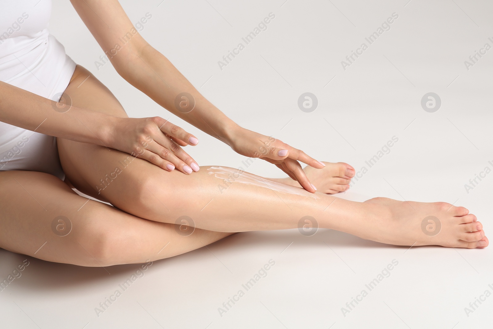 Photo of Woman applying body cream onto her smooth legs on white background, closeup