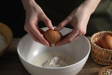 Photo of Making bread. Woman adding egg into dough at wooden table on dark background, closeup