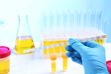 Photo of Laboratory assistant holding litmus paper for analysis over table, closeup