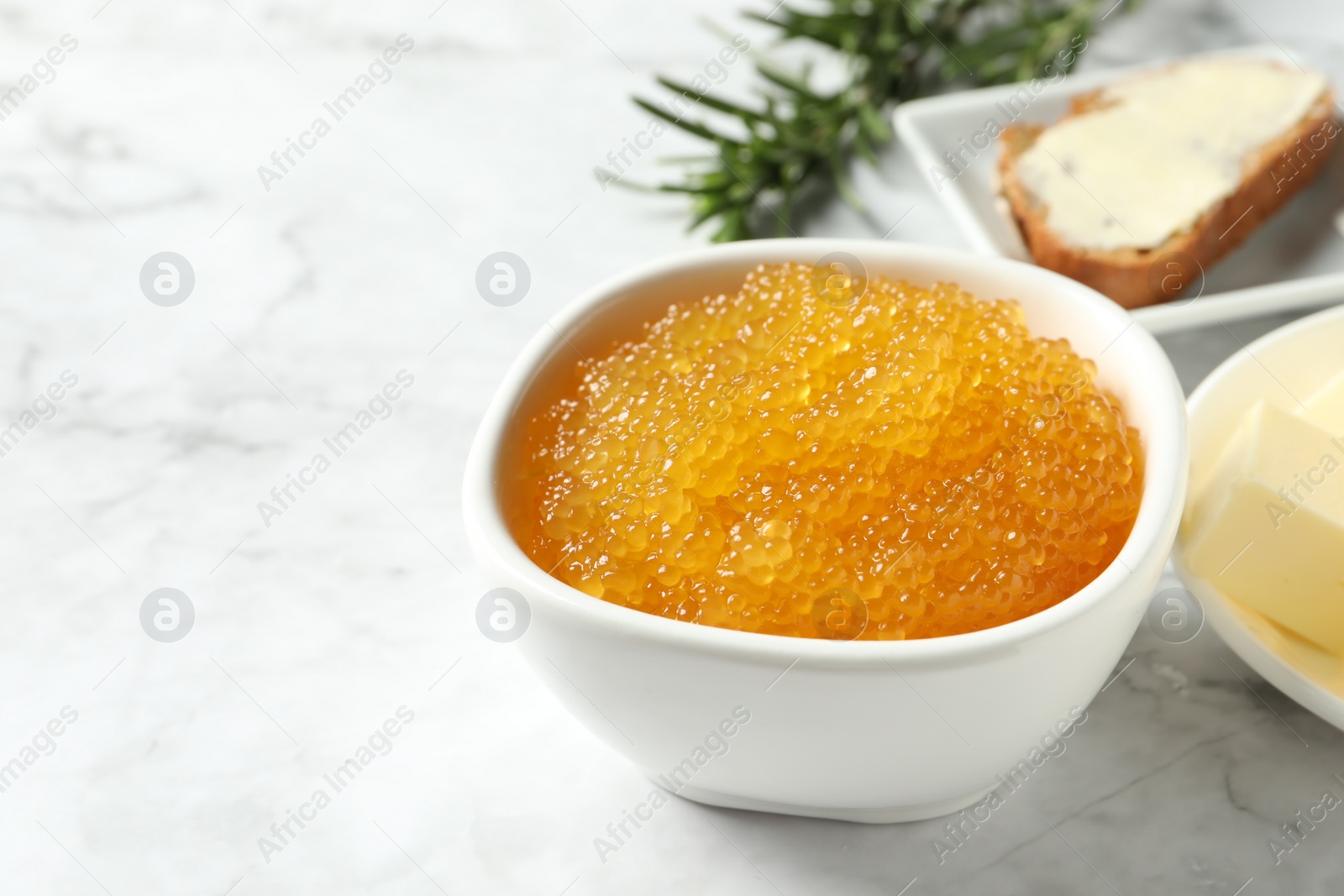 Photo of Fresh pike caviar in bowl, bread, rosemary and butter on white marble table, closeup. Space for text