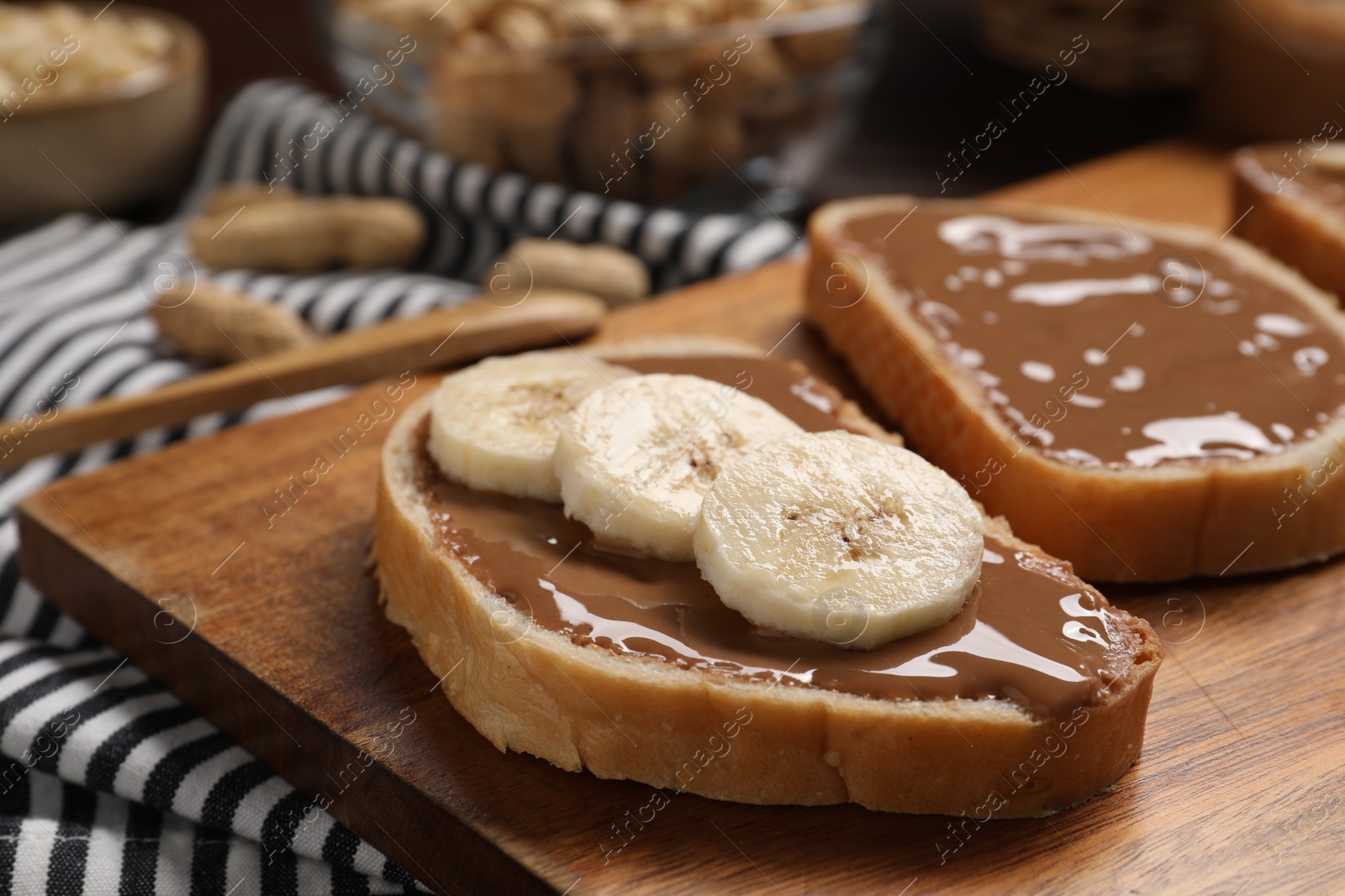 Photo of Toasts with tasty nut butter and banana slices on wooden board, closeup