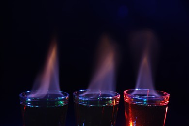 Photo of Flaming alcohol drink in shot glasses on dark background, closeup