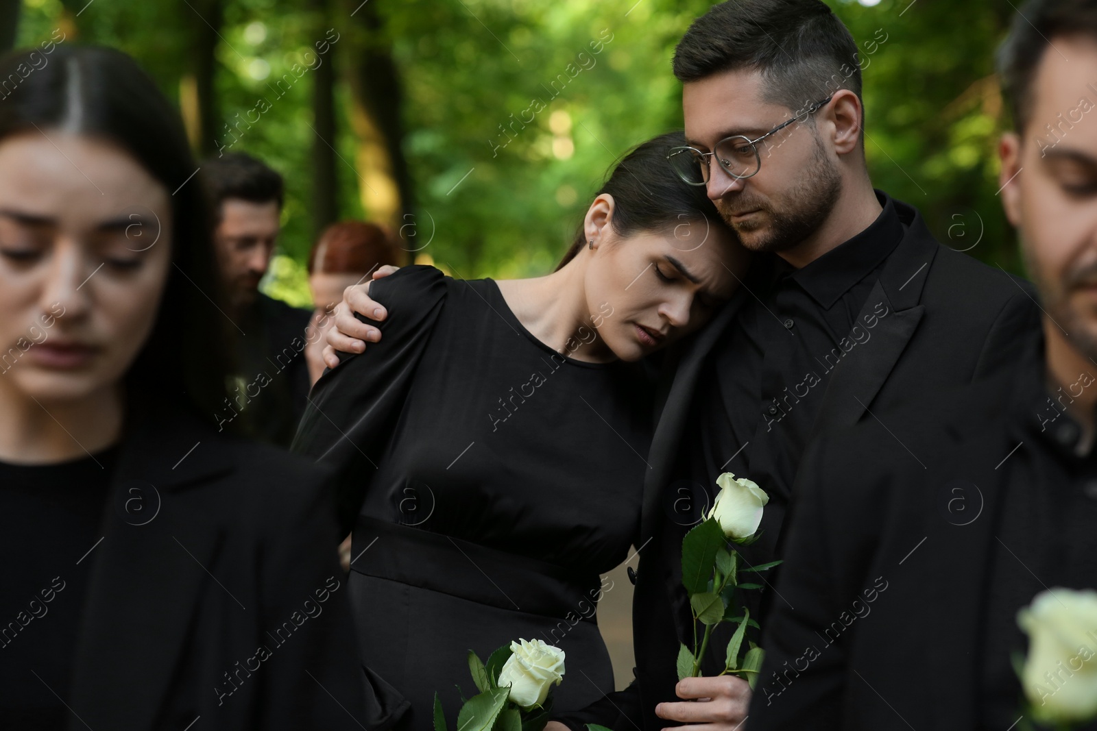 Photo of Funeral ceremony. Sad people with white rose flowers mourning outdoors