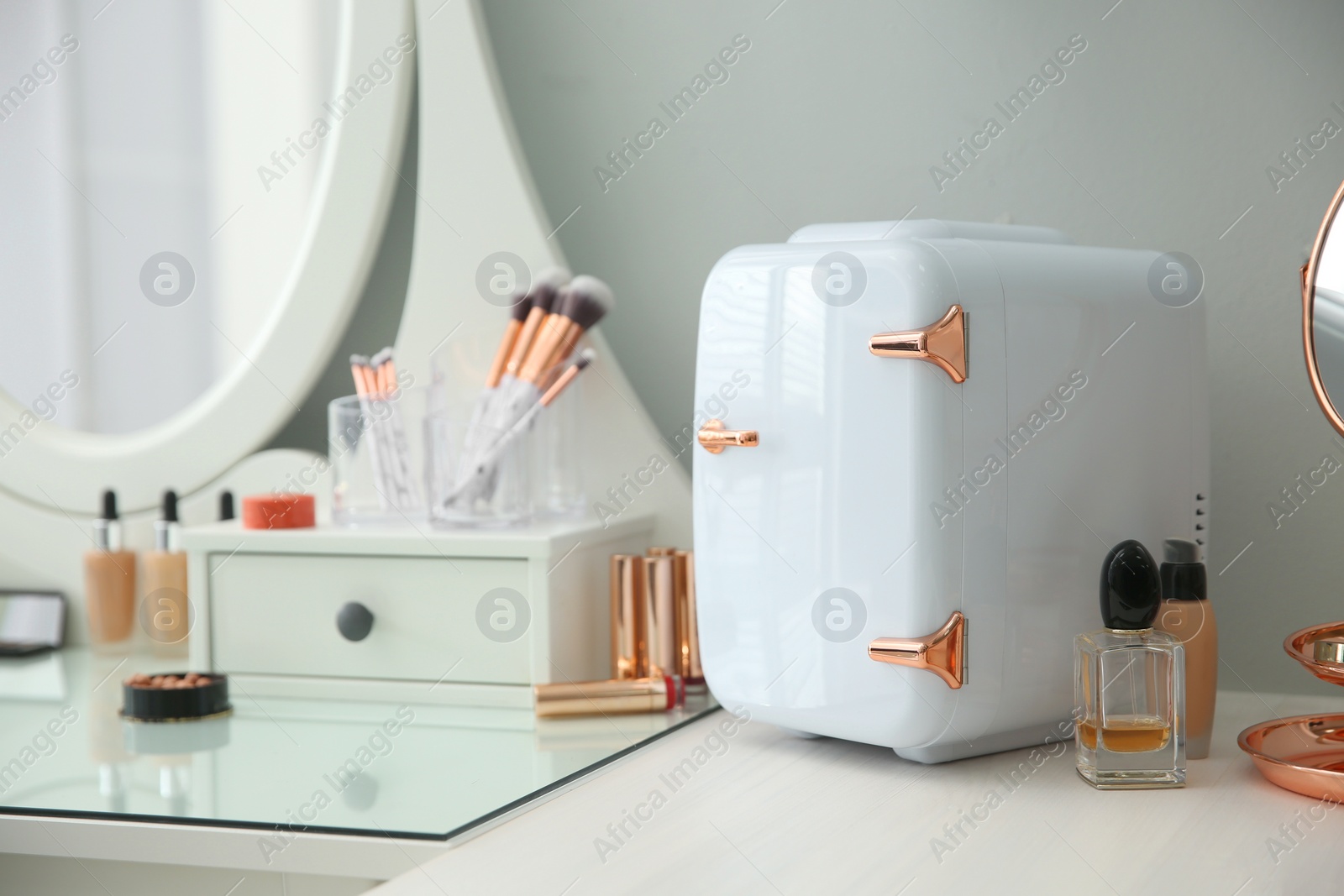 Photo of Cosmetics refrigerator and skin care products on white vanity table indoors