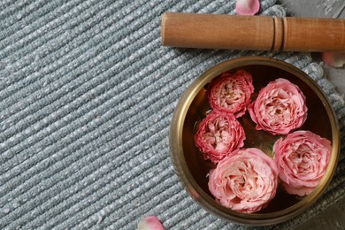 Tibetan singing bowl with water, beautiful roses and mallet on mat, top view. Space for text