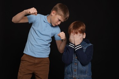 Photo of Boy with clenched fists bullying scared kid on black background