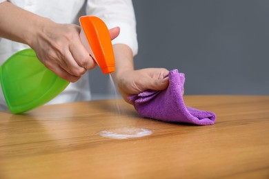 Woman cleaning wooden table with rag and detergent indoors, closeup