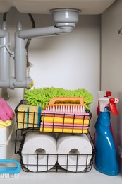 Photo of Open under sink cabinet with different cleaning supplies in kitchen