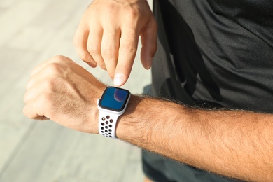 Photo of Man using modern smart watch during training outdoors, closeup