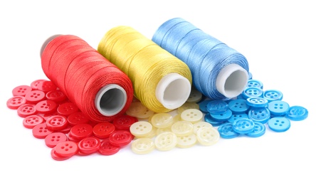 Set of colorful sewing threads and matching buttons on white background