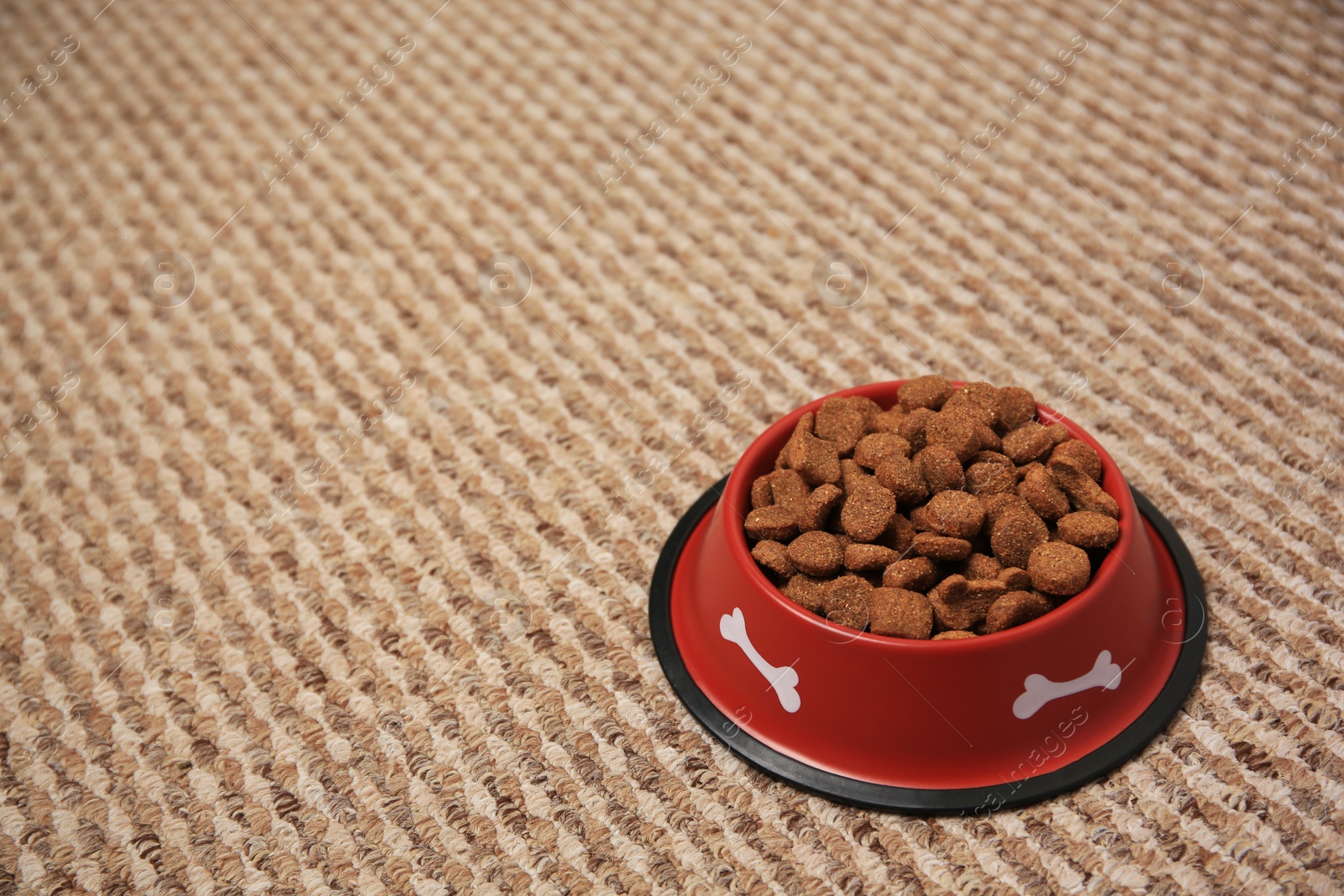 Photo of Dry dog food in feeding bowl on soft carpet. Space for text