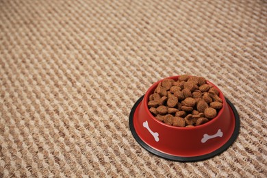 Photo of Dry dog food in feeding bowl on soft carpet. Space for text