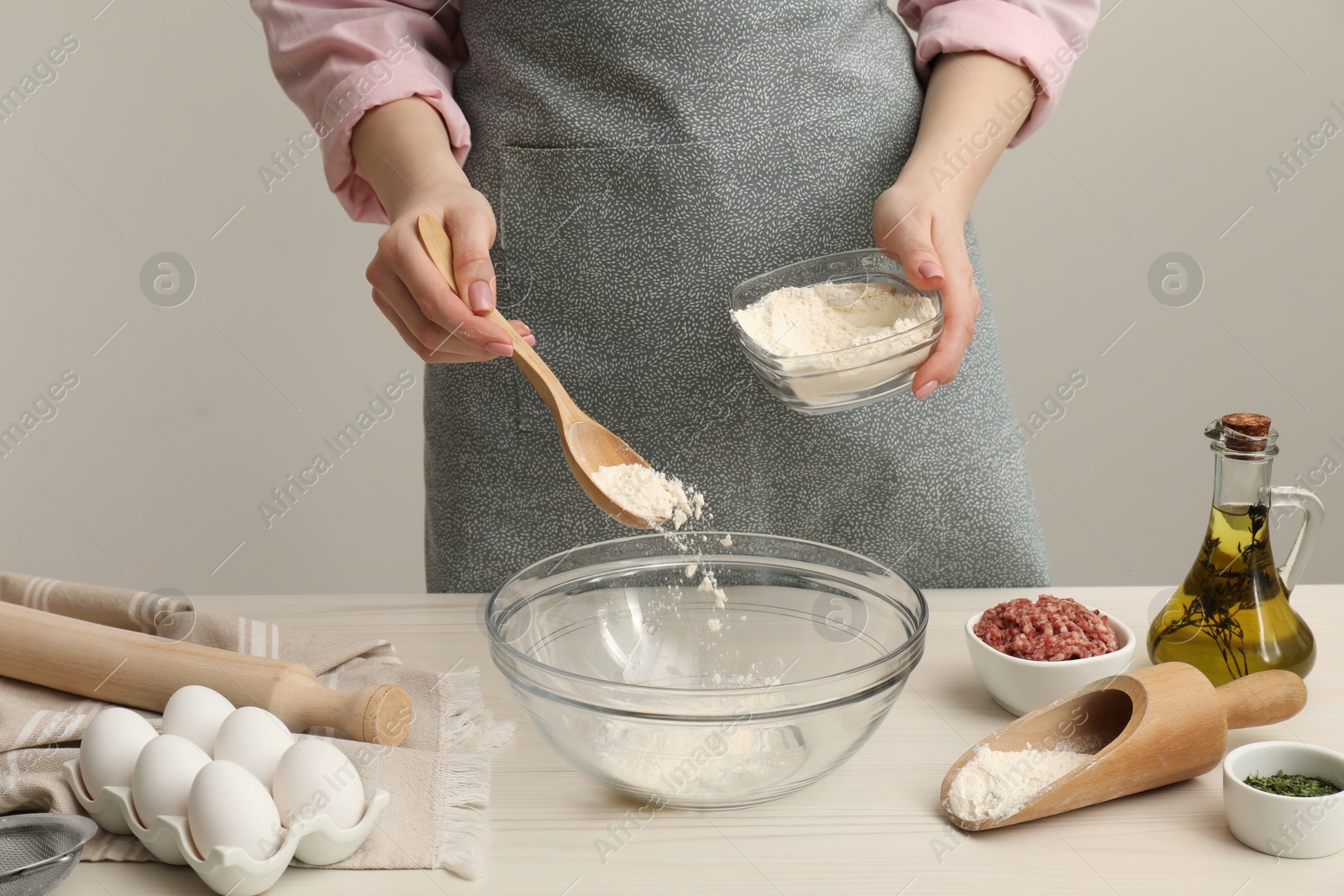 Photo of Woman putting flour into bowl at white wooden table, closeup