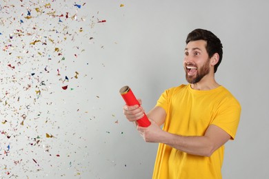 Emotional man blowing up party popper on light grey background