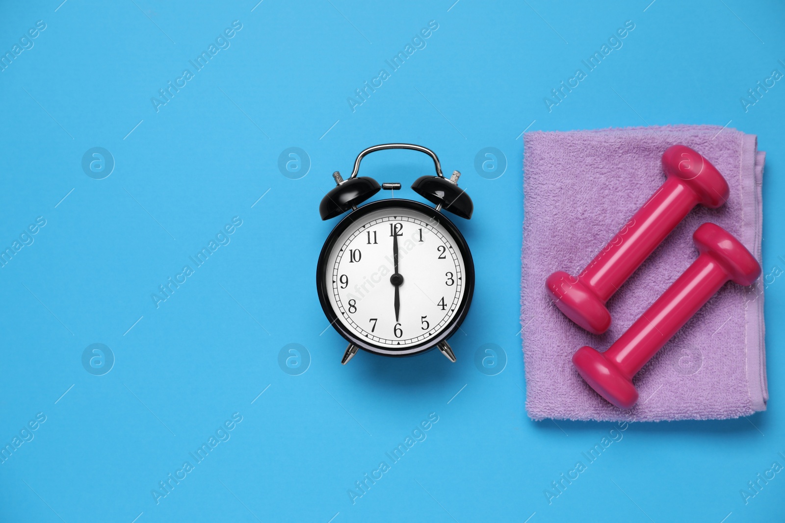 Photo of Alarm clock, towel and dumbbells on light blue background, flat lay with space for text. Morning exercise