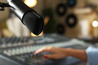 Photo of Woman working with professional mixing console in modern radio studio, focus on microphone. Space for text