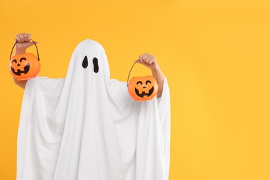 Woman in white ghost costume holding pumpkin buckets on yellow background, space for text. Halloween celebration
