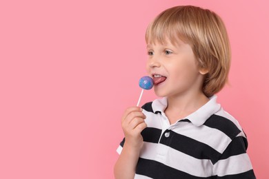 Photo of Cute little boy licking lollipop on pink background, space for text
