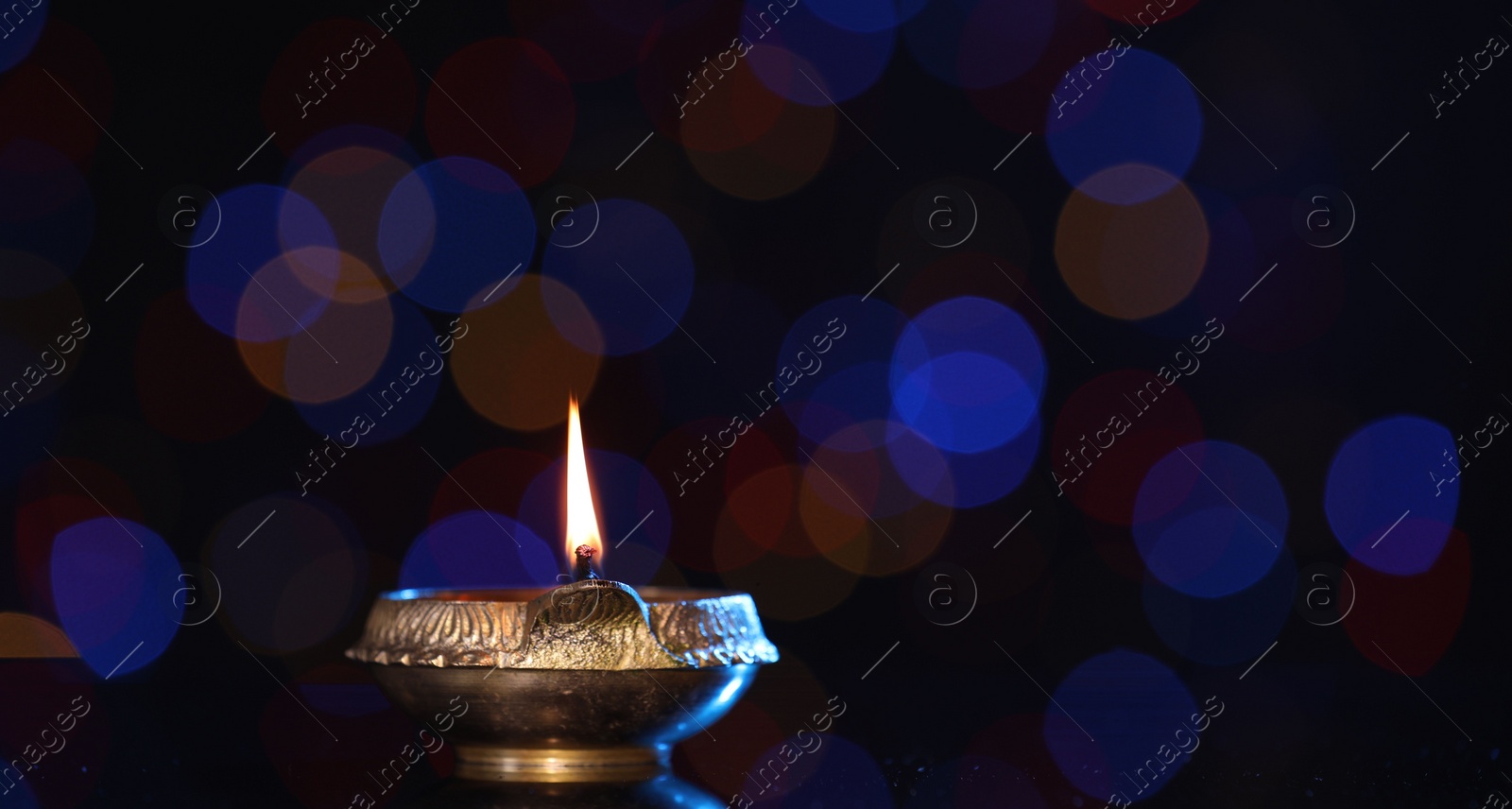 Photo of Lit diya on dark background with blurred lights, space for text. Diwali lamp