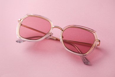 Photo of New stylish sunglasses on pink background, closeup. Fashionable accessory