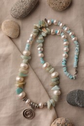 Beautiful necklace with gemstones and different stones on light cloth, flat lay