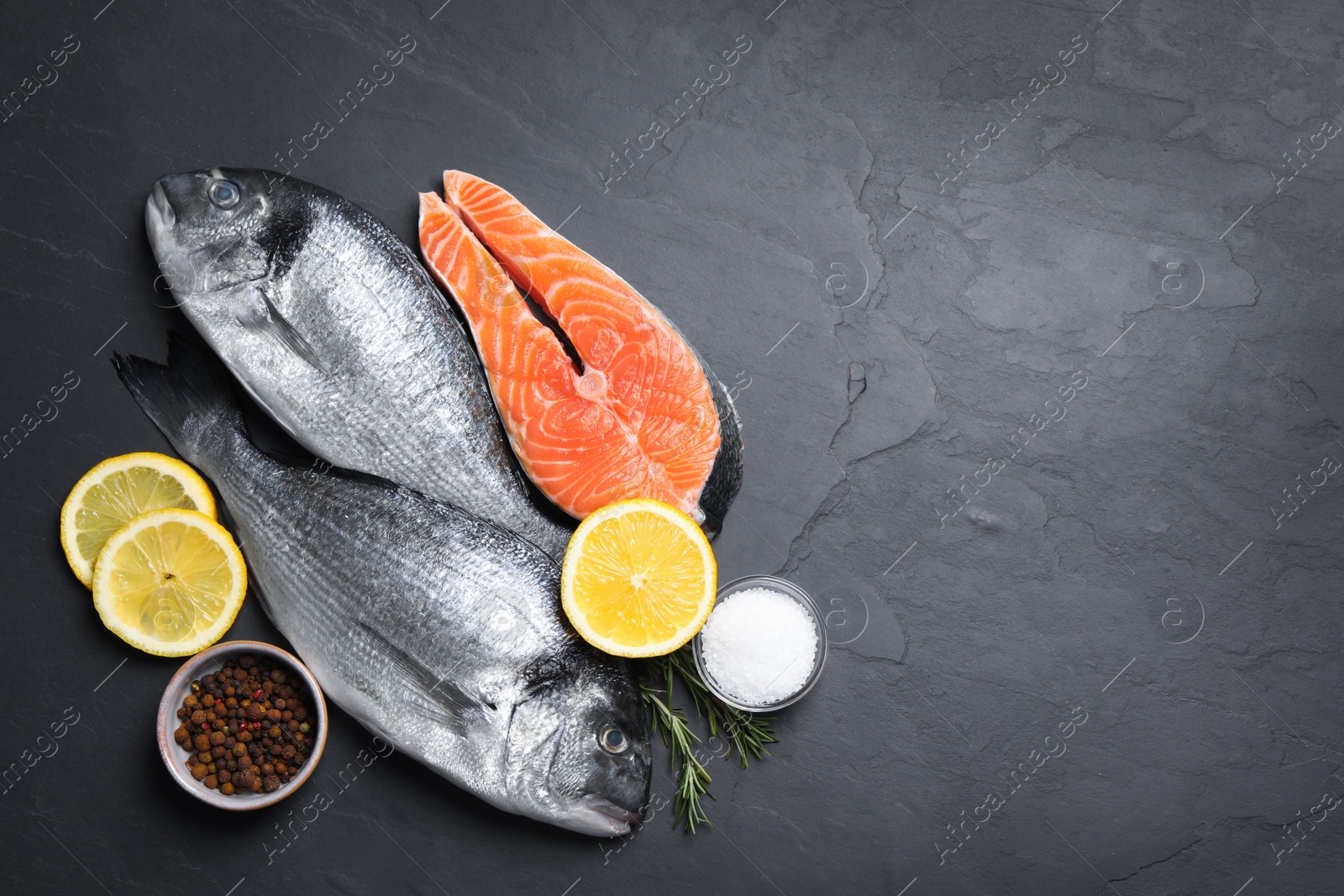 Photo of Fresh dorado fish, salmon and ingredients on black slate background, flat lay. Space for text