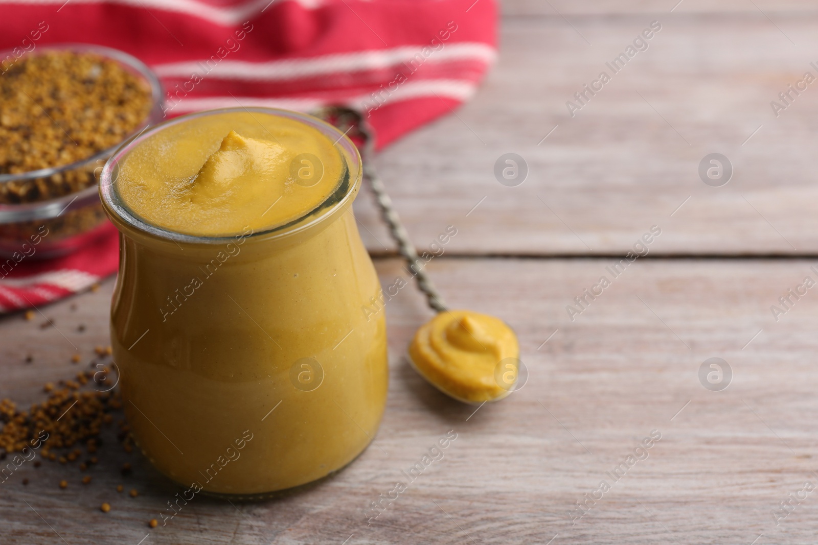 Photo of Jar and spoon with tasty mustard sauce on wooden table, space for text