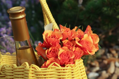 Yellow wicker bag with beautiful roses and bottle of wine outdoors