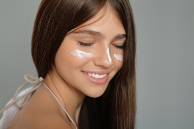 Teenage girl with sun protection cream on her face against grey background, closeup