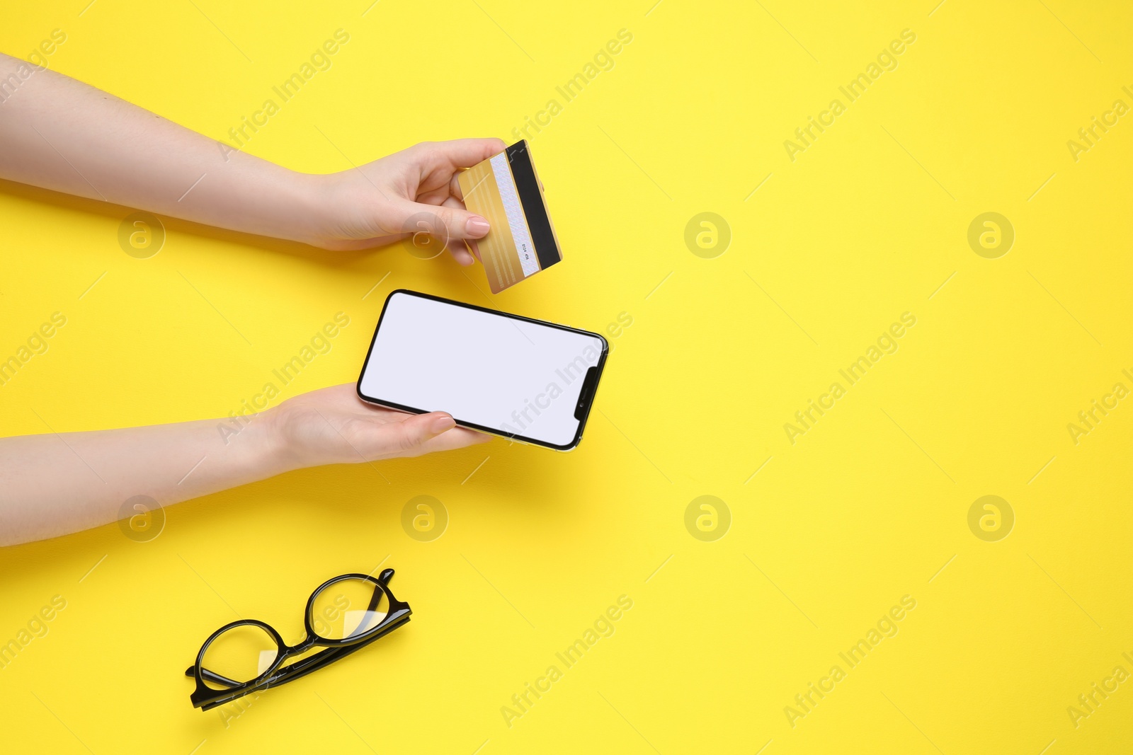 Photo of Online payment. Woman with smartphone, credit card and glasses on yellow background, top view. Space for text