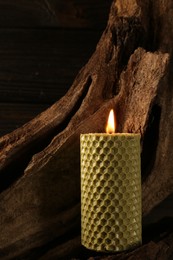 Beautiful burning beeswax candle on snag near wooden wall