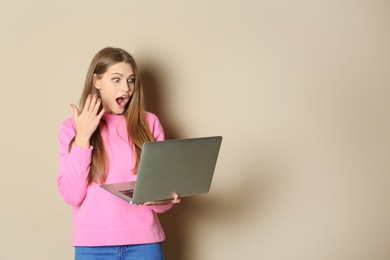 Emotional young woman with laptop celebrating victory on color background. Space for text