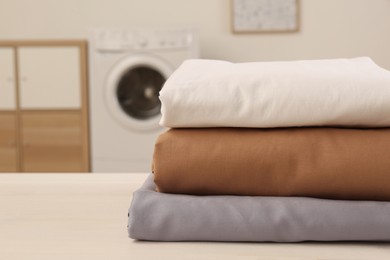 Photo of Stack of clean bed linens on white wooden table in laundry room