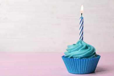 Photo of Delicious birthday cupcake with cream and burning candle on pink table. Space for text