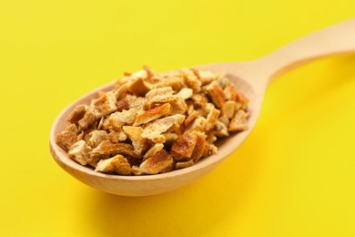 Photo of Spoon with dried orange zest seasoning on yellow background, closeup