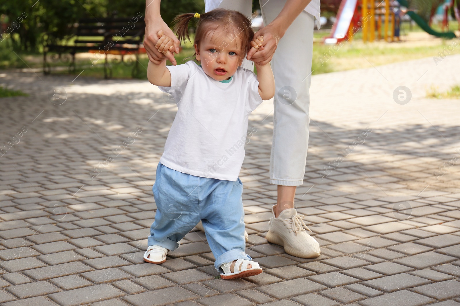 Photo of Mother supporting daughter while she learning to walk outdoors, closeup