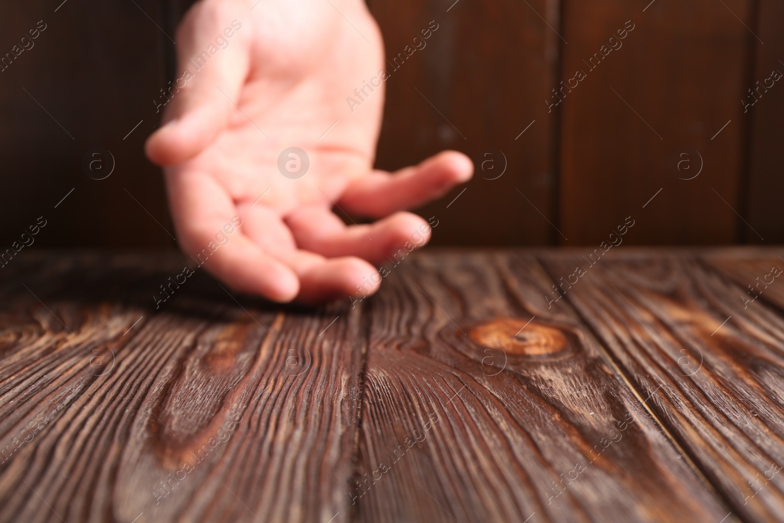 Photo of Man holding hand above wooden table, selective focus. Space for text