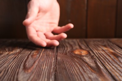 Photo of Man holding hand above wooden table, selective focus. Space for text