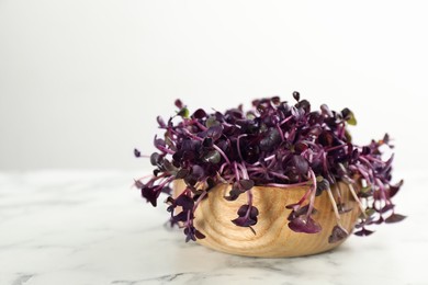 Photo of Fresh radish microgreens in wooden bowl on white marble table, closeup. Space for text